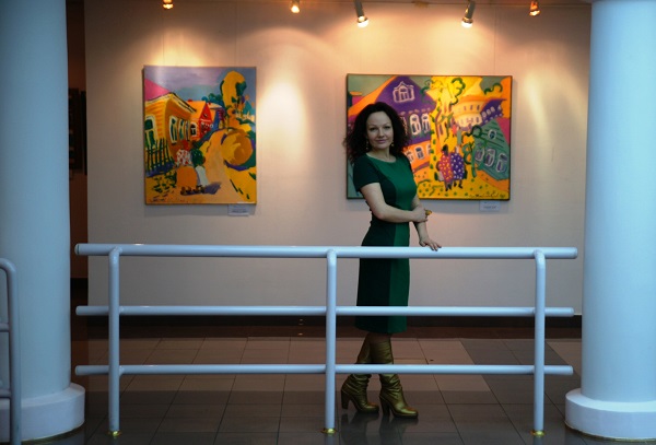 Художник Дарья Багринцева на фоне картины  Ольги Мотовиловой-Комовой в галерее "На Чистых Прудах"